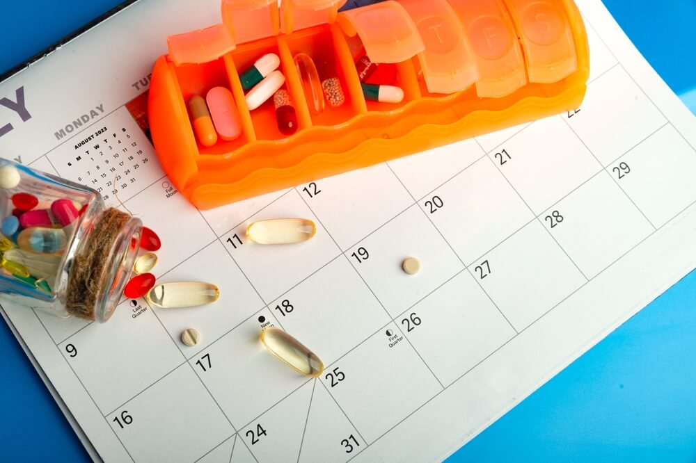 am pm pill organiser on top of a calendar with a jar of vitamins
